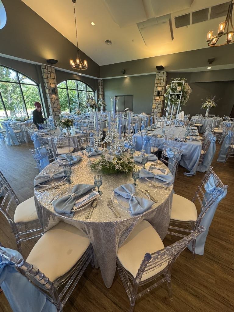 Blue and silver guest tables with floral centerpieces and clear chairs