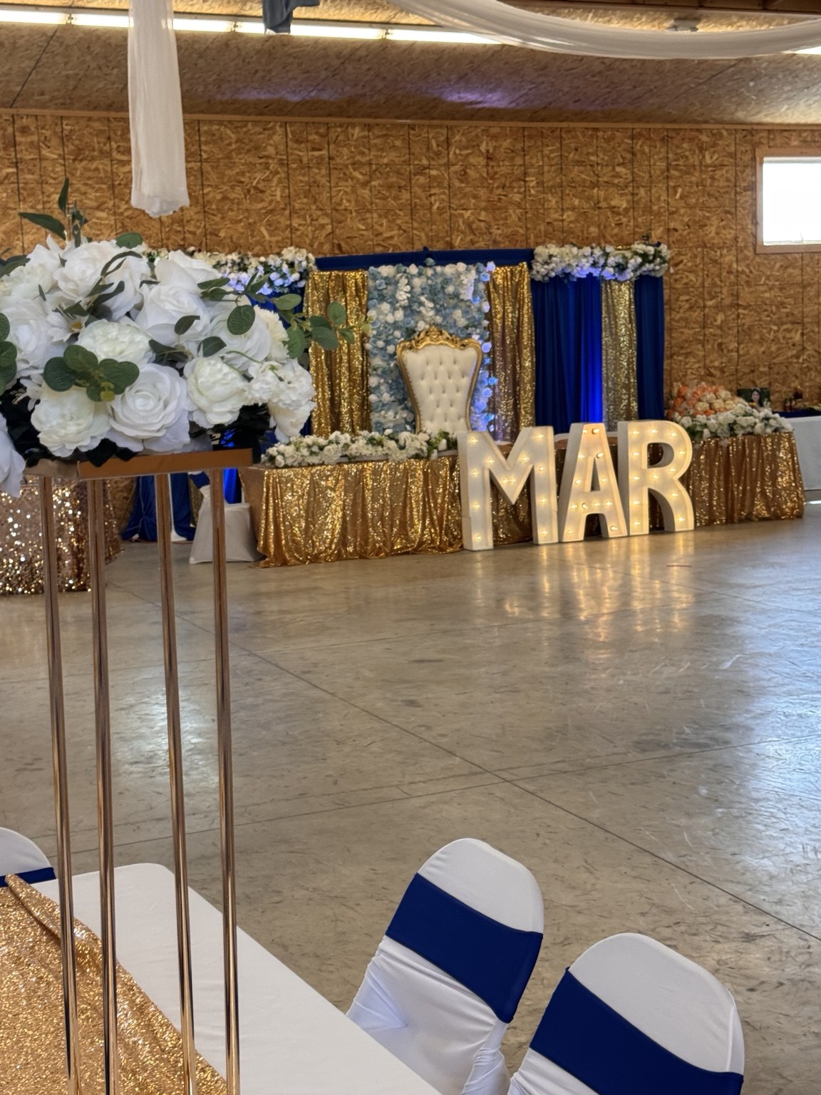 Blue and gold celebration stage with white flowers and illuminated marquee letters