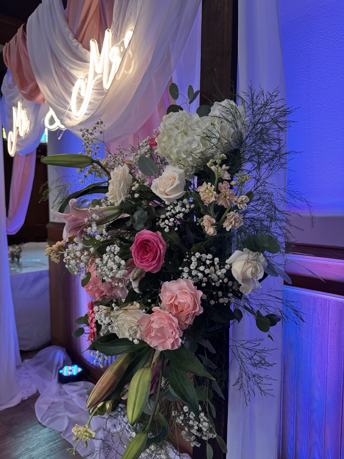 Pink and white flowers with greenery on a softly draped wedding arch