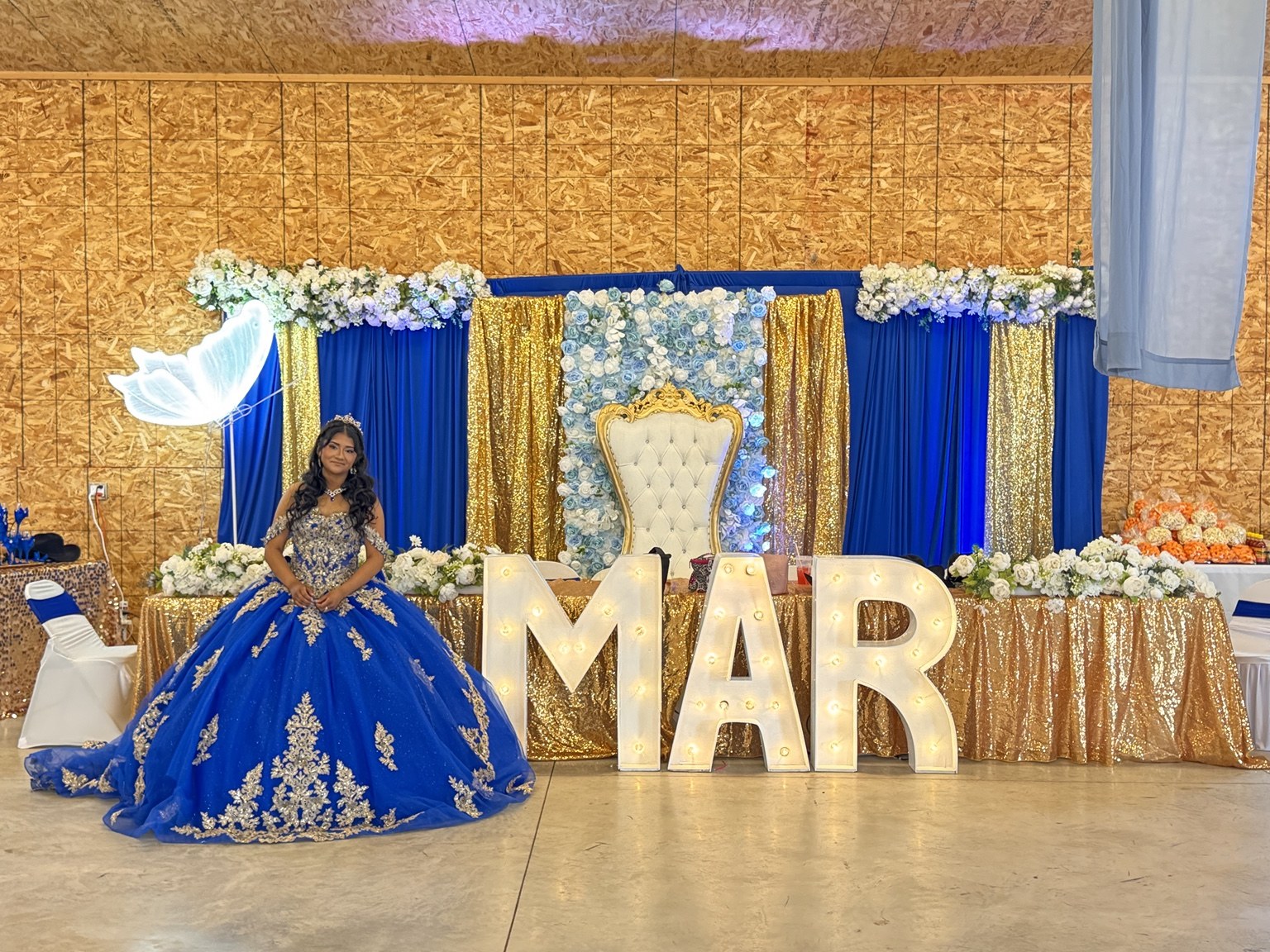 Royal blue and gold quinceañera backdrop with white throne and illuminated MAR letters