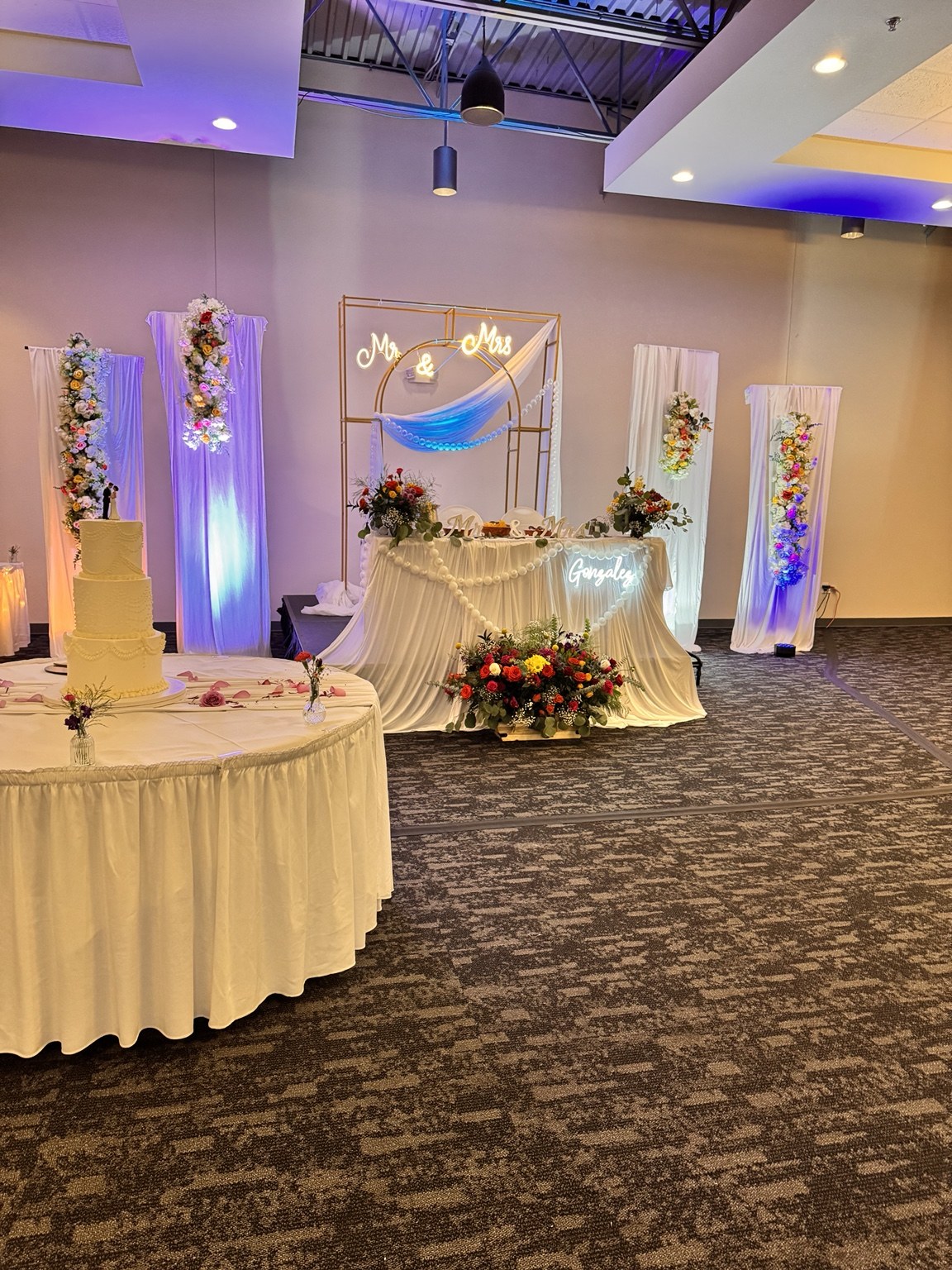 Wedding sweetheart table with white draping, flowers and softly lit backdrop panels