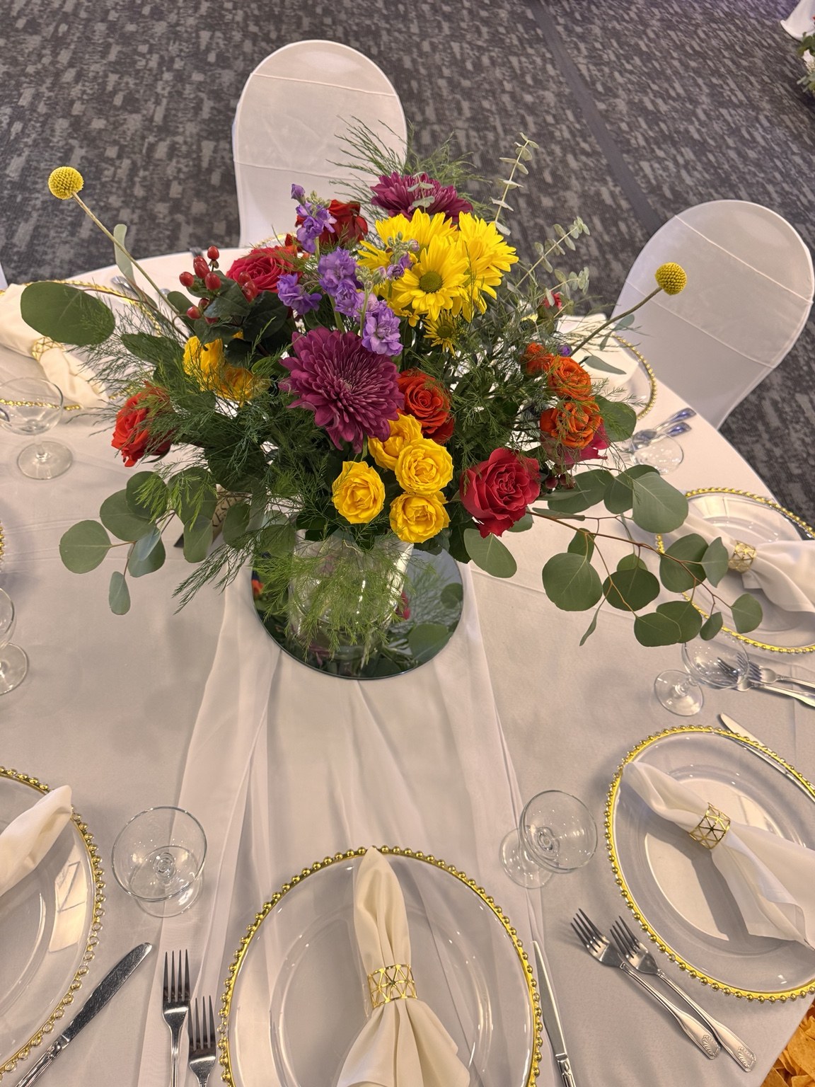 Colorful floral centerpiece with eucalyptus and clear gold-rimmed chargers