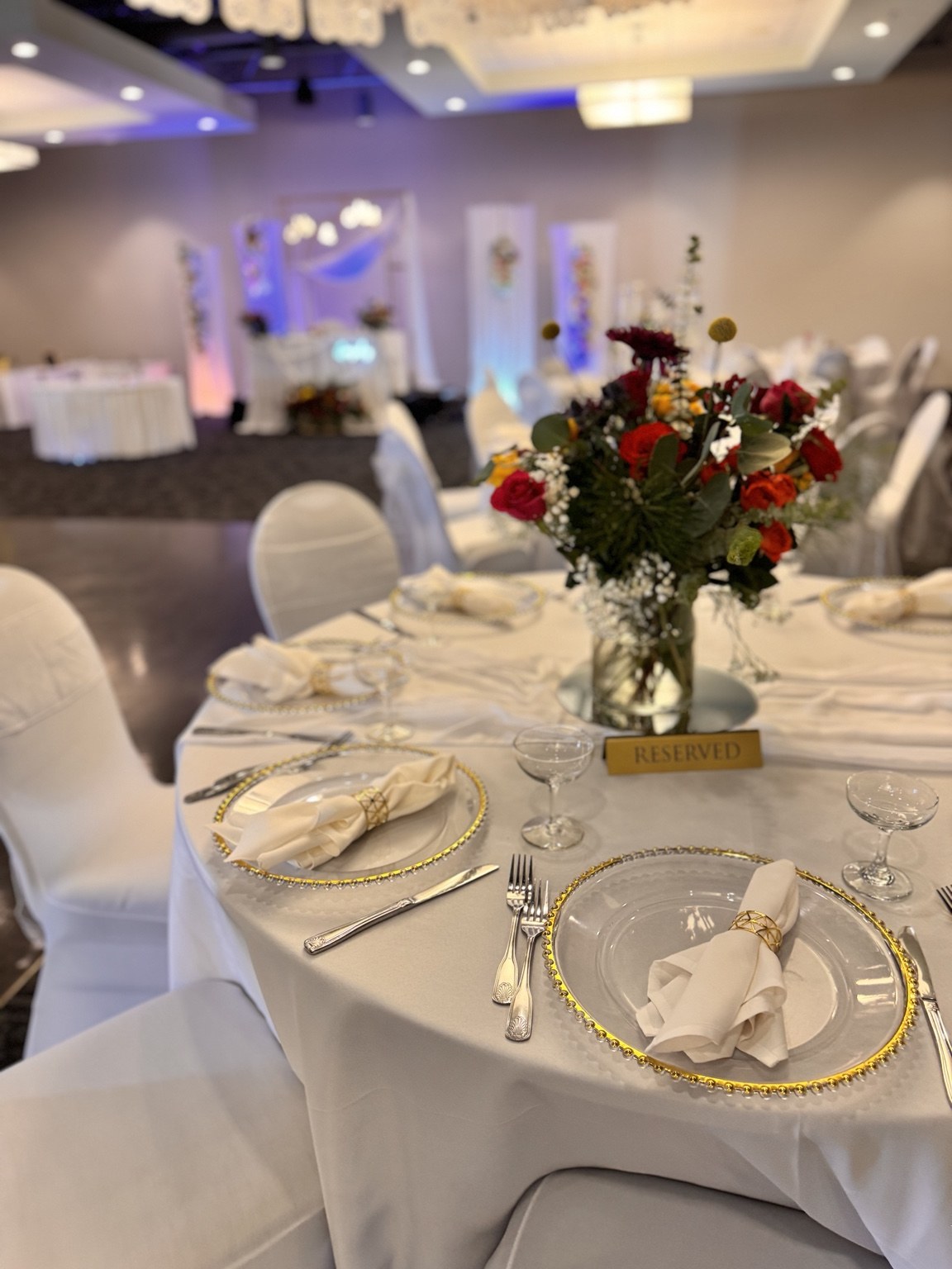 White wedding guest table with colorful centerpiece and gold-rimmed chargers