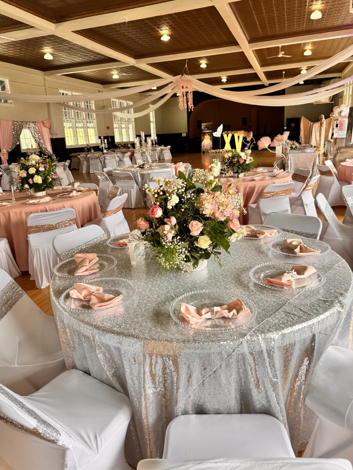 Quinceañera reception with blush and silver tables, floral centerpieces and ceiling draping