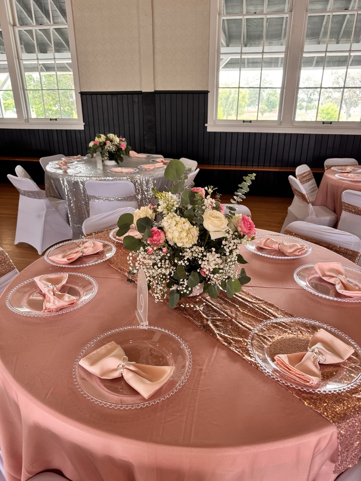 Blush tablecloth with clear chargers, bow napkins and a pink and white floral centerpiece