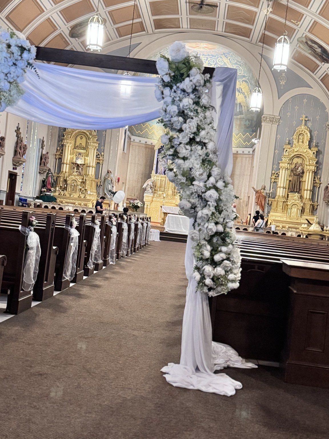 Church wedding arch with flowing white draping and white floral arrangements