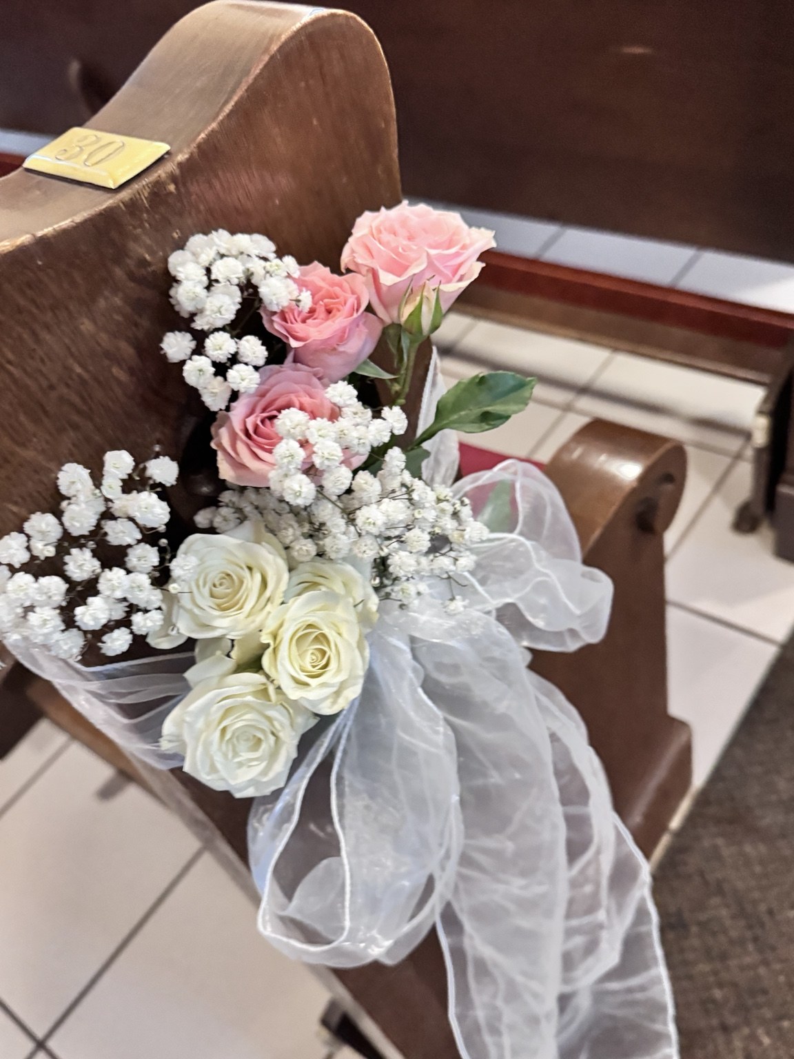 Wedding pew flowers with pink and white roses, babys breath and a tulle bow