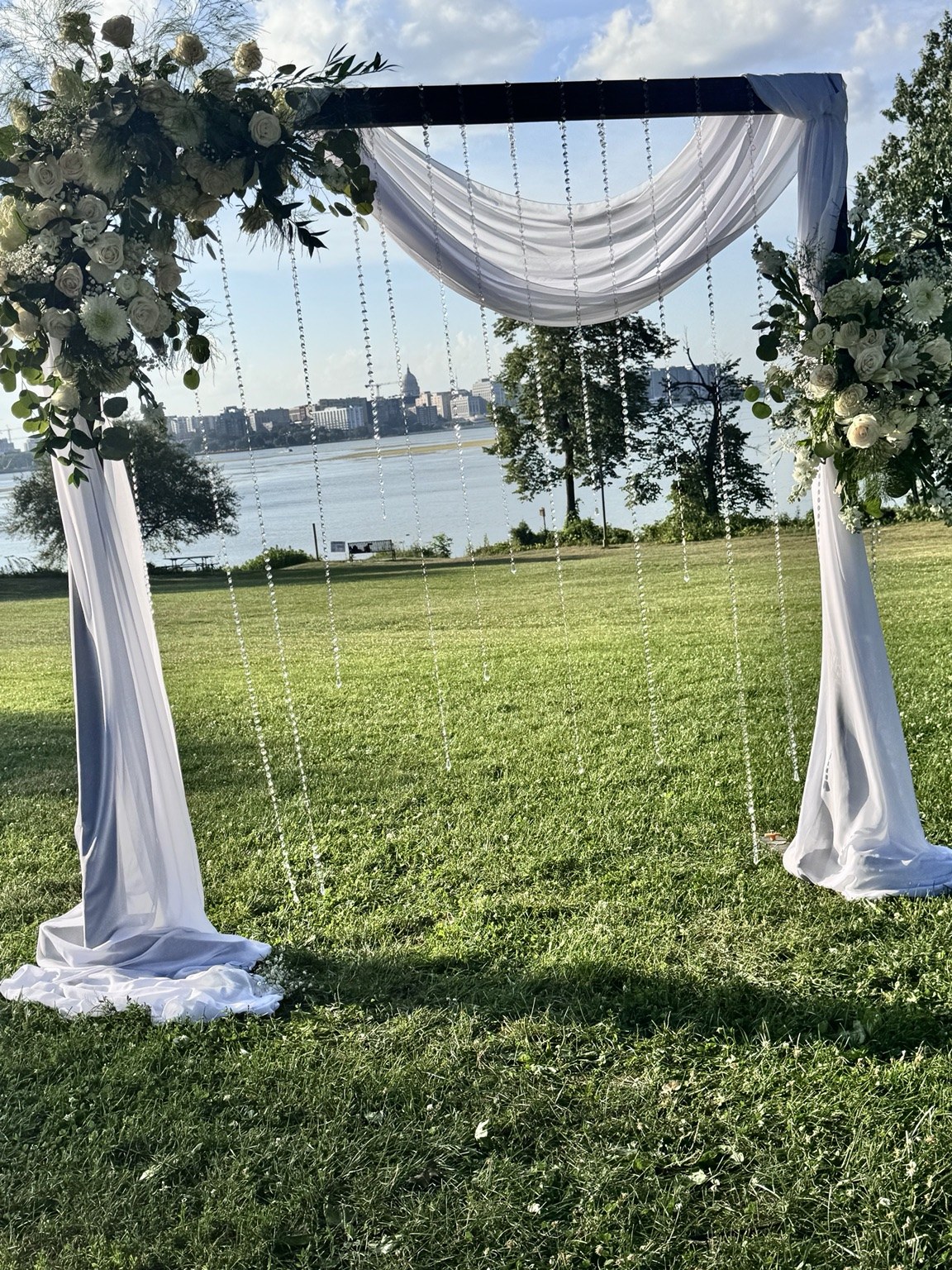 White draped floral wedding arch on a lawn overlooking the water
