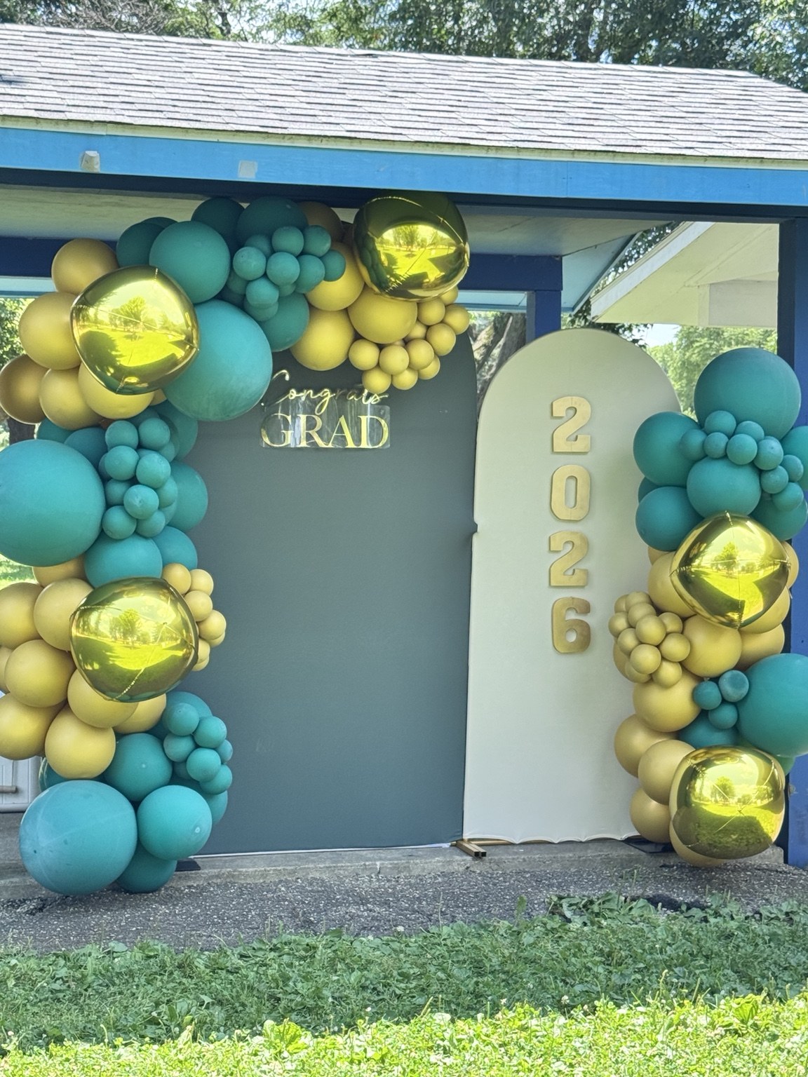 Outdoor graduation photo backdrop with teal and gold balloons and 2026 panel