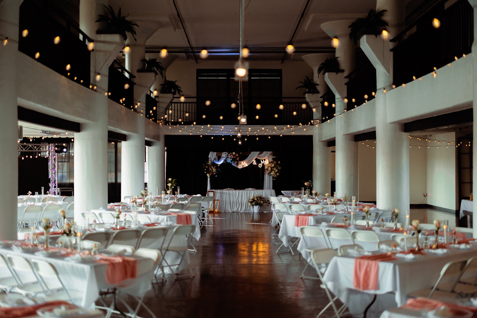 Wedding reception with white chairs, coral table accents and overhead string lights