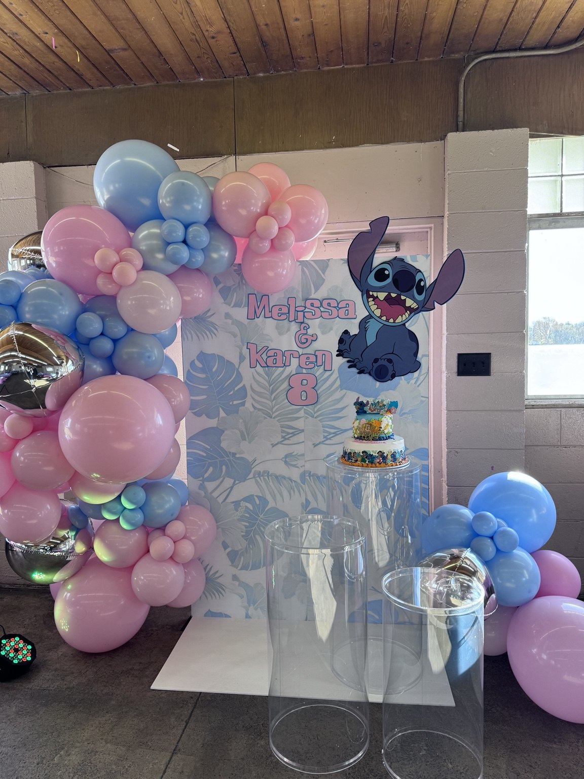 Birthday cake display with pink and blue balloons and a personalized Stitch theme