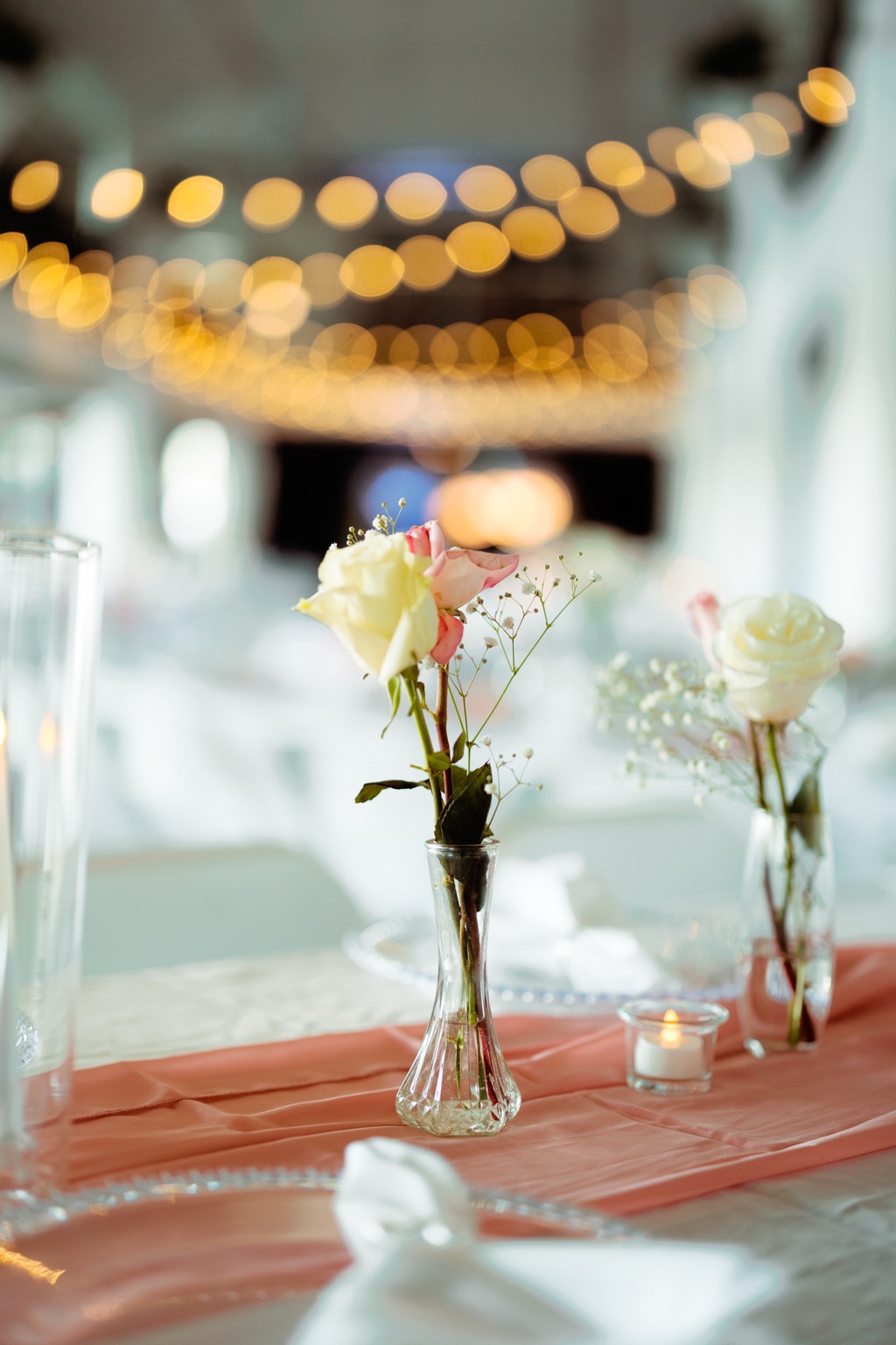 Wedding guest table with small floral vases and warm string lights in the background