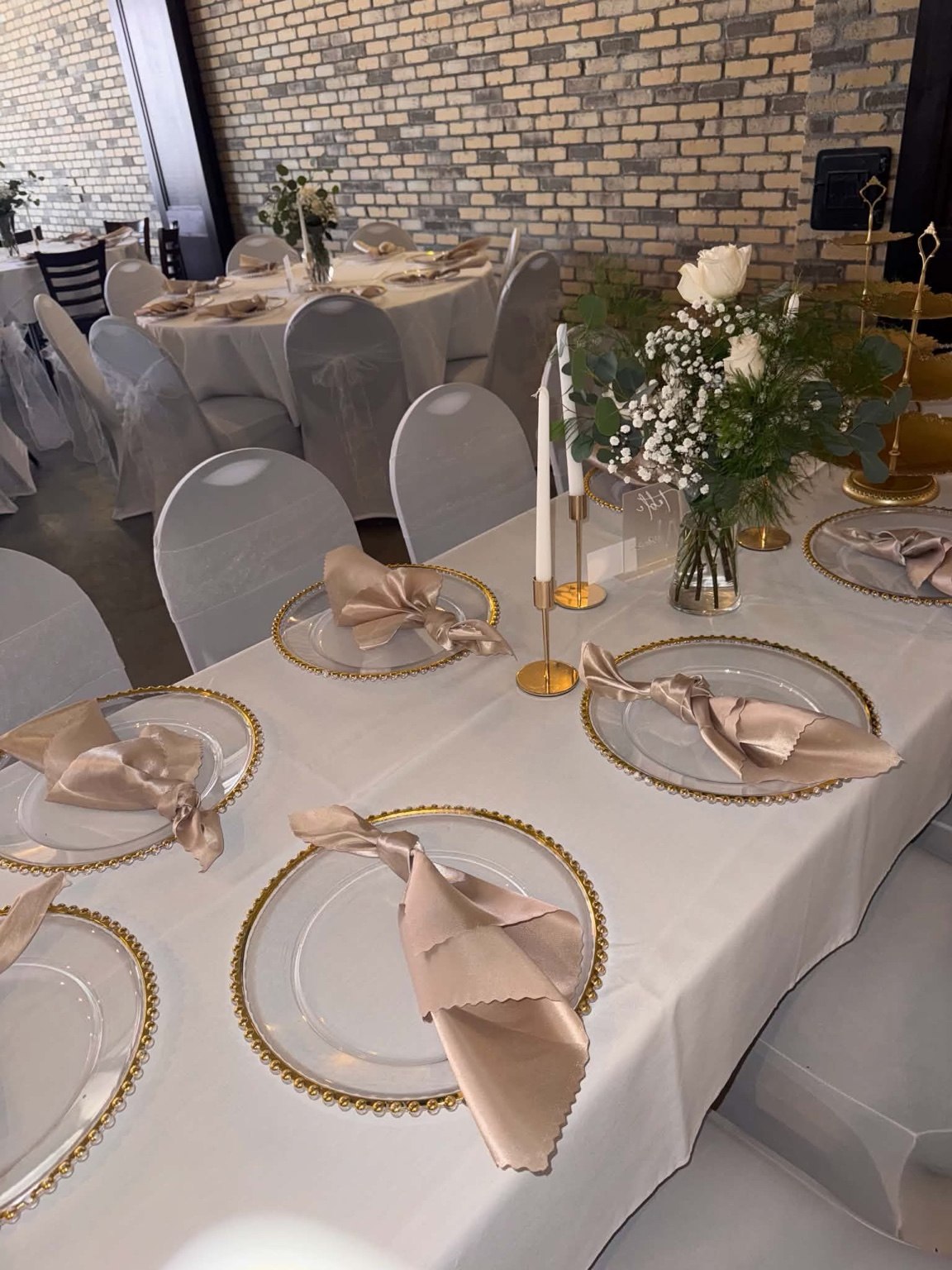 White reception table with gold chargers, neutral napkins and delicate flowers