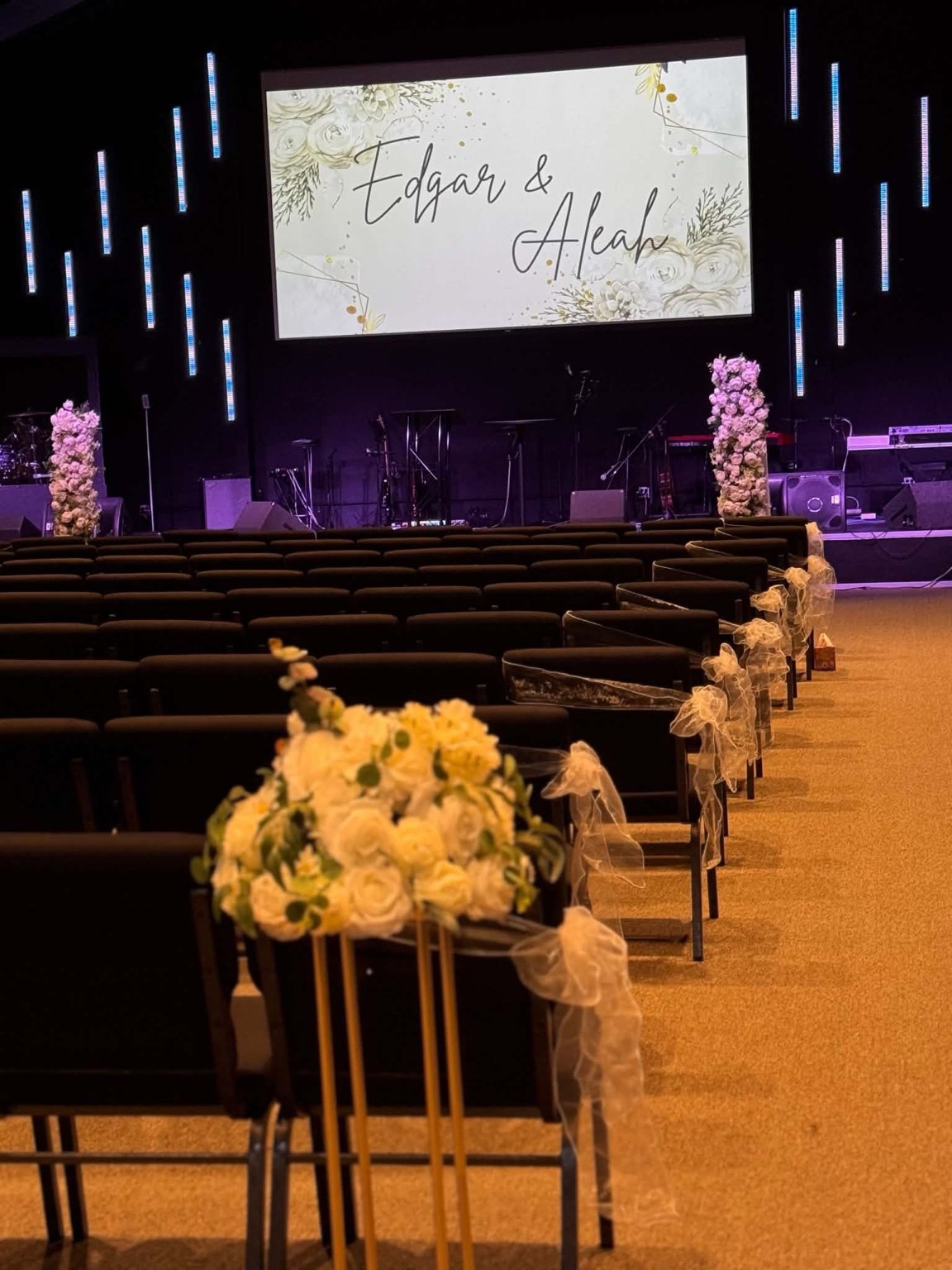 Wedding ceremony aisle lined with white floral arrangements on gold stands